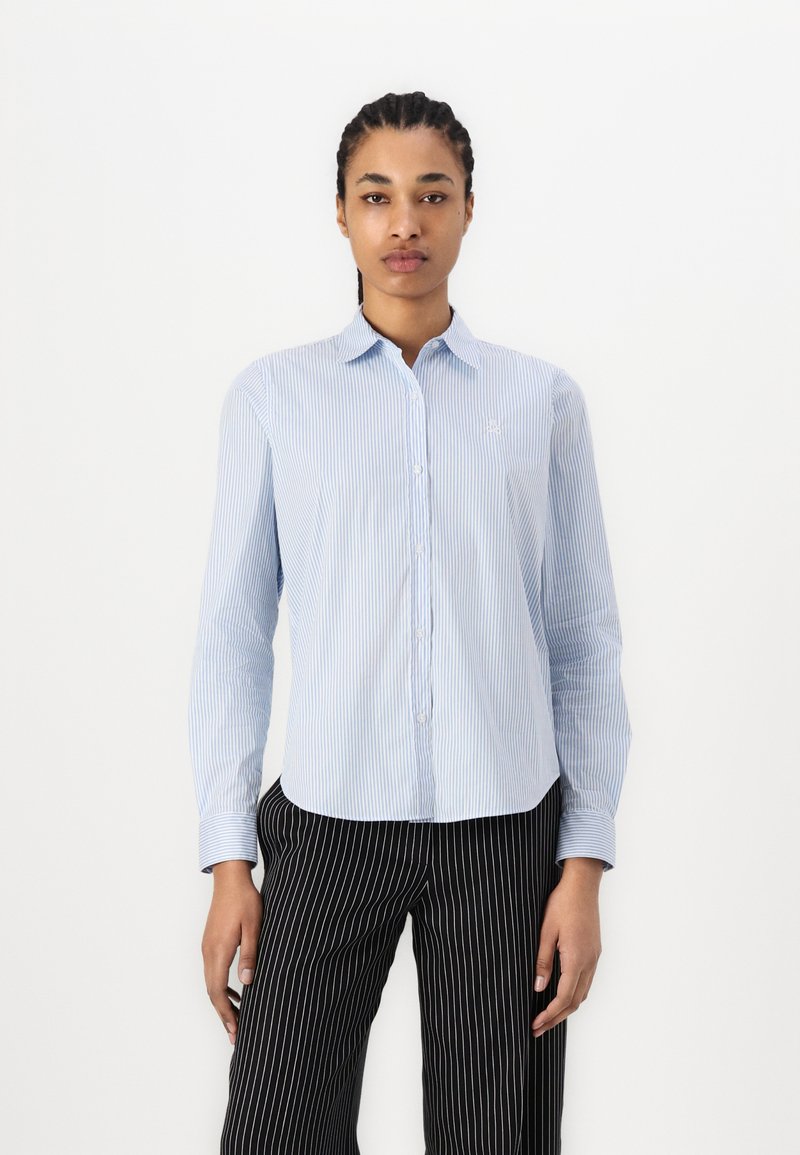 Camicia a maniche lunghe a righe azzurro chiaro con collo alla camicia, presenta un piccolo logo ricamato sul lato sinistro del petto. Pantaloni a righe nere.