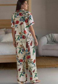 Cămașă cu imprimeu floral, cu mâneci scurte și pantaloni largi, de culoare crem, cu accente roșii, albastre și verzi. Țesătură ușoară cu o textură netedă.