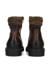 Par de botas de cuero y gamuza marrones vistas desde atrás, con suelas de goma negras y cierres de cremallera en los lados internos.