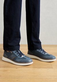 Blaue Sneaker aus einer Kombination von strukturiertem Mesh und glattem Leder. Weiße Gummisohle, Schnürdesign und seitliches Reißverschlussdetail.