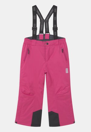 Pantalon imperméable rose avec bretelles noires réglables, poches latérales zippées, renforts noirs aux genoux et fermetures à pression aux ourlets.