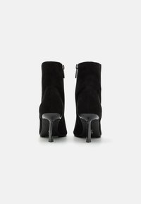 Czarne zamszowe botki za kostkę z ostrym noskiem, wysokim obcasem typu stiletto i bocznym zamkiem błyskawicznym. Gładka tekstura z eleganckim, dopasowanym fasonem.