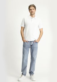Polo bianco a maniche corte, abbinato a jeans in denim azzurro chiaro e sneaker bianche. Stile casual, design semplice, senza motivi visibili.
