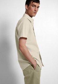 Beige skjorte med korte ermer og kragehals, laget av lett stoff. Kombinert med lysegrønne bukser som viser et uformelt design.