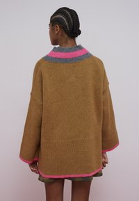 Prevelik rjav pulover iz pletenine z visokim ovratnikom, s sivimi in roza črtami. Ohlapni rokavi in rebrast rob dodajata teksturo.
