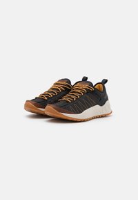 Zapatos deportivos negros con cordones naranjas, parte superior de tela texturizada, suela de goma y entresuela blanca. Cuenta con una lengüeta en la parte trasera para facilitar el calzado.