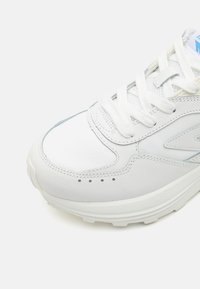 Baskets blanches avec une tige en cuir et des accents bleu clair, bout arrondi, lacets blancs plats et une semelle en caoutchouc texturé pour une bonne adhérence.