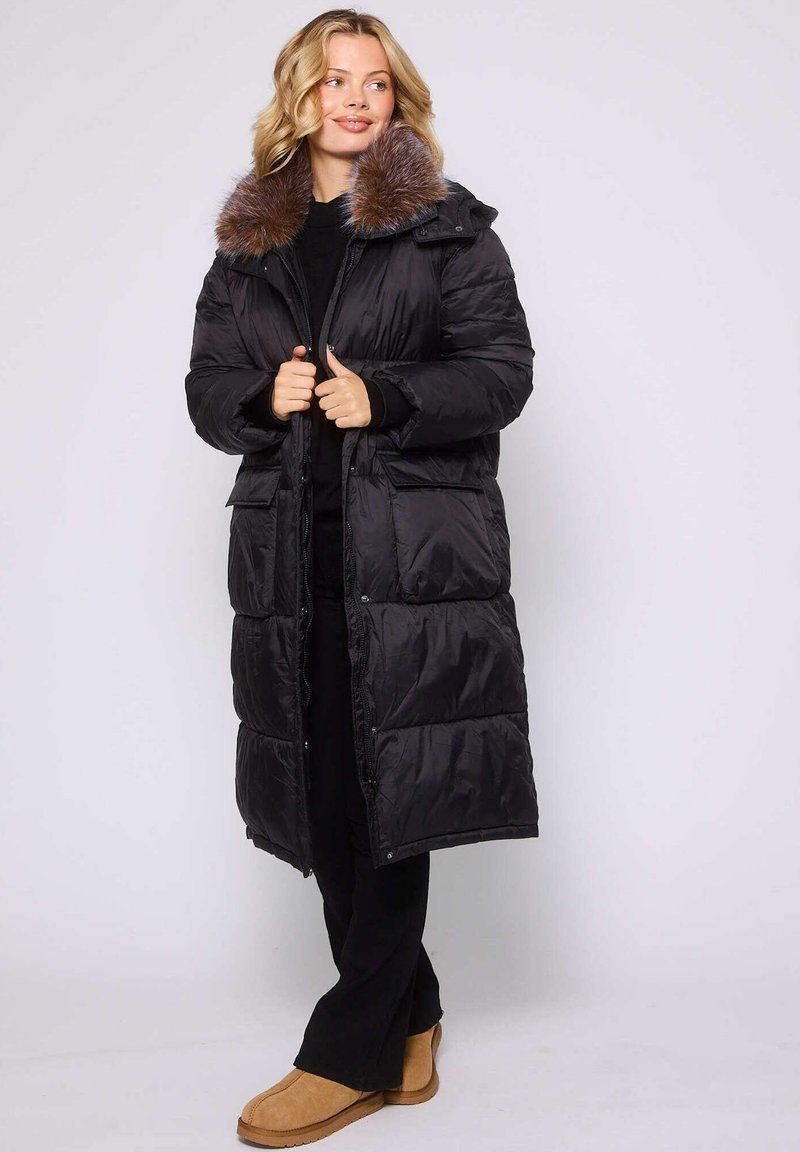 Czarna puchowa kurtka z kapturem wykończonym futrem, z zapięciem na zamek, dwoma przednimi kieszeniami i długością do kolan. Gładka, błyszcząca tekstura.