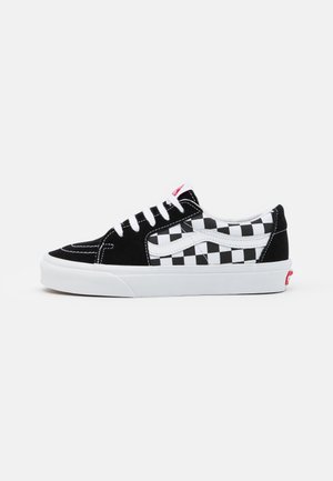 Schwarz-weiße Low-Top-Sneaker mit einem Karomuster, aus Wildleder, weißen Schnürsenkeln und einer weißen Gummisohle mit roten Akzenten.