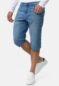 Shorts de denim en azul, con un corte relajado, dobladillos enrollados y diseño de cinco bolsillos. Combinados con zapatillas blancas, que muestran un estilo minimalista.