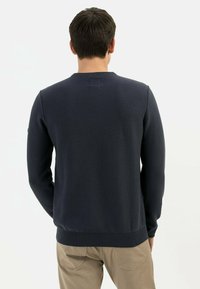 Pull en laine bleu marine avec un col rond, des poignets et un ourlet côtelés, présentant un motif texturé à l'arrière et un petit détail logo.