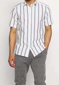 Wit shirt met korte mouwen en horizontale donkergrijze strepen, knoopsluiting aan de voorkant, lichtgewicht stof, gecombineerd met zwart-witte geruite broek.