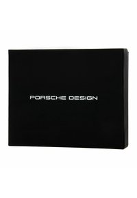 Scatola rettangolare nera con finitura opaca, dotata di lettering bianco "PORSCHE DESIGN" centrato sul fronte. Design elegante e minimale.