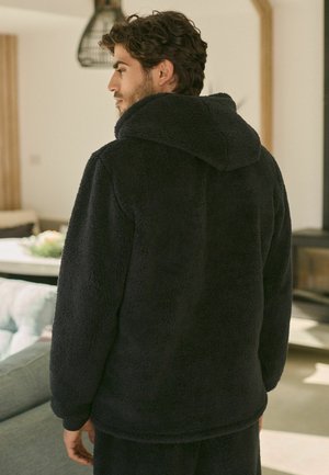 Black fleece hoodie with a textured, soft exterior, featuring a spacious hood and long sleeves, worn over matching pants.