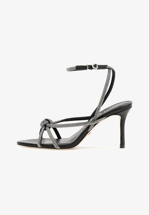 Black high-heeled sandal featuring a knotted front, rhinestone accents on the straps, and a slender stiletto heel. Smooth texture.