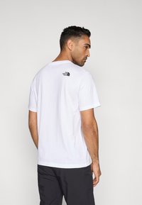Λευκό βαμβακερό t-shirt με κοντά μανίκια, που φέρει το μαύρο λογότυπο The North Face στο πάνω μέρος της πλάτης. Ομαλή υφή και κανονική εφαρμογή.