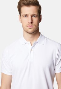 Biała koszulka polo z klasycznym kołnierzykiem, krótkimi rękawami i zapięciem na dwa guziki. Posiada gładki, teksturowany materiał.