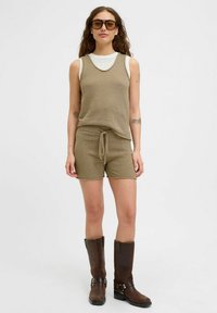 Khaki pletená souprava obsahující top bez rukávů a kraťasy s nastavitelným šňůrkovým páskem. V kombinaci s hnědými koženými kozačkami po kolena.