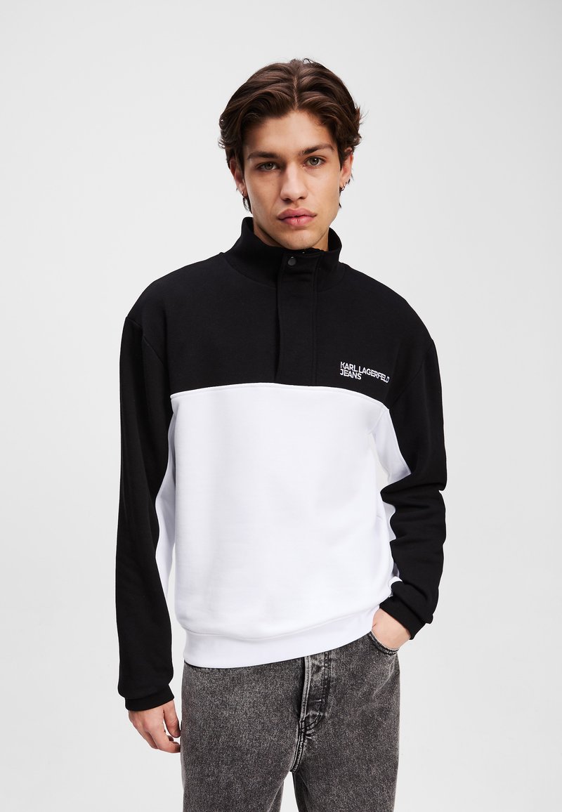 Pullover in bianco e nero con col alto, dotato di un logo sul petto, maniche lunghe e un tessuto morbido e testurizzato.