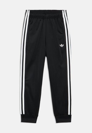 Pantaloni atletici neri con vita elastica, tre strisce bianche lungo i lati, caviglie risvoltate e piccolo logo Adidas trefoil bianco sulla coscia sinistra.