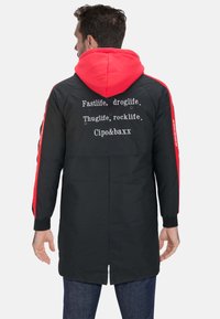 Schwarze Jacke mit roten Akzenten und Kapuze. Auf der Rückseite steht der Text: "Fastlife, droglife. Thuglife, rocklife. Cipo&baXX." Lange Ärmel.