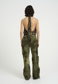 Top a laccio nero e marrone con stampa leopardata, abbinato a pantaloni cargo tie-dye verde oliva con tasche laterali e cintura a catena.