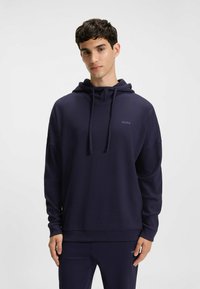 Granatowa bluza z kapturem o teksturowanym wykończeniu, ze sznurkami przy szyi i subtelnym logo na klatce piersiowej, z luźnym krojem i długimi rękawami.