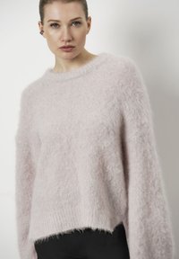 Roze, donzige trui van zacht materiaal, met een wijde halslijn en lange, losse mouwen met een iets verkorte zoom.