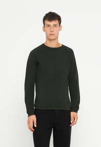 Pulover lung cu mânecă lungă de culoare verde închis, cu un design texturat de tricot și guler rotund. Material neted, formă ajustată și tivuri și manșete ribbate.
