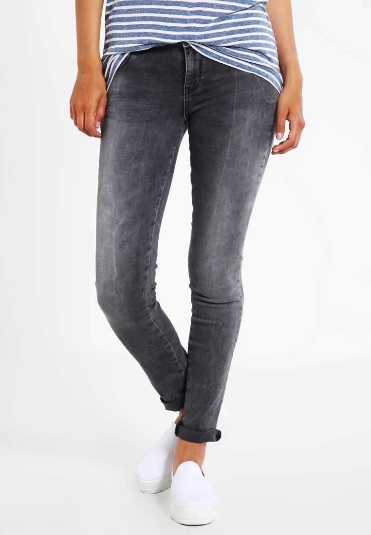 Vaqueros skinny grises con un lavado desgastado, que presentan un ajuste slim y puños enrollados. Combinados con zapatillas blancas sin cordones y una blusa a rayas azul.