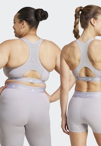 Twee vrouwen in lichtgrijze sportkleding, die een achterontwerp met een uitsnede en textuurstof tonen. De tailleband heeft een "TECHFIT" logo.