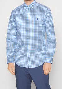 Blå och vit rutmönstrad skjorta med knappar, långa ärmar, spridd krage och en liten logotyp på bröstet. Slät bomullstyg.