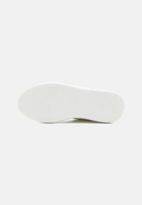 Semelle de chaussure en caoutchouc blanc présentant un motif en chevron pour une meilleure adhérence. Texture lisse avec une forme arrondie et des accents de marque minimalistes.