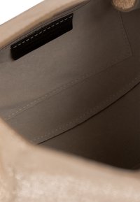 Interno di una borsa in pelle beige con una consistenza morbida, caratterizzato da un'etichetta nera e cuciture visibili lungo le cuciture.