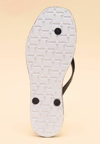 Black flip-flop with a textured white rubber sole featuring a patterned tread design, accented by two black circular pads for stability.