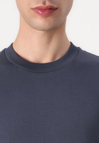 Námorně modré bavlněné tričko s ribbovaným kulatým výstřihem. Hladká textura, těsně přiléhající design a decentní prošití kolem límce.