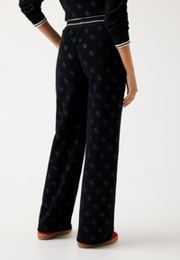 Zwarte wijde broek van corduroy met een subtiel patroon, voorzien van een contrasterende witte tailleband en rode schoenen.