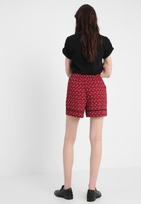 Röda mönstrade shorts med lös passform, prydda med vita hjärtan och svart kant; kombinerade med en enfärgad svart topp med kort ärm.