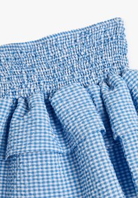 Tissu à carreaux bleus et blancs avec texture froncée à la taille, montrant des volants et un matériau en coton léger.