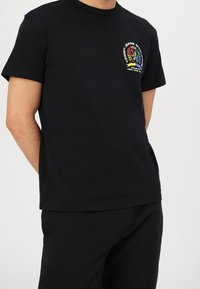 Svart bomull t-shirt med en färgglad logotyp på bröstet. Tröjan har korta ärmar och en klassisk rund halsringning.