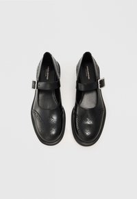 Scarpe Mary Jane in pelle nera con punta rotonda, dettagli perforati, bordo a scallop e una cinghia regolabile con fibbia argento.