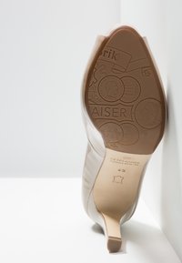 Chaussure à talon haut beige avec un dessus en cuir lisse et un bout pointu. La semelle présente des motifs en relief et des détails de marque.
