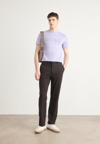 T-shirt violet clair avec le logo "BOSS", pantalon noir et baskets blanches avec des semelles beiges. Comprend un sac à épaule gris.