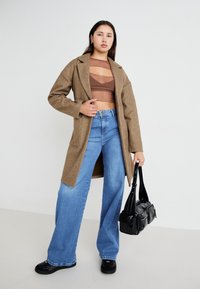 Abrigo marrón estructurado sobre un top corto marrón, combinado con pantalones vaqueros anchos azules y calzado negro. Accesorio: bolso negro de hombro.
