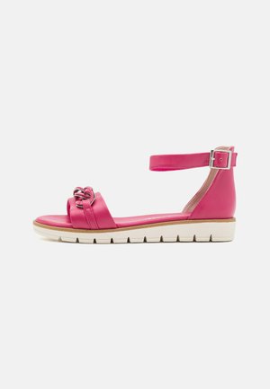 Sandal en cuir rose avec un bout rond, une sangle de cheville ajustable, un accent métallique à l'avant et une semelle blanche contrastante avec une texture antidérapante.