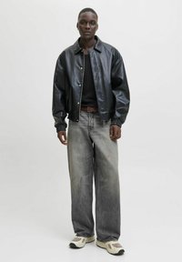 Veste bomber en cuir noir avec des poignets en élasthanne, associée à un jean en denim gris taille haute et des baskets beiges imposantes. T-shirt noir ajusté en dessous.