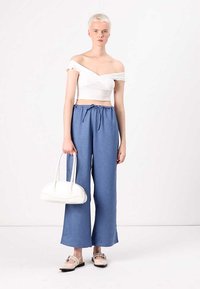 Bela off-shoulder skrajšani top, modri široki hlače z vrvico, smetana ročna torba in svetlo bež čevlji z ravnim podplatom.