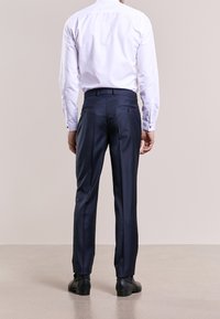 Pantaloni a fantasia navy con vestibilità sartoriale, dotati di una parte frontale liscia, tasche laterali e due tasche posteriori. Abbinati a una camicia bianca.
