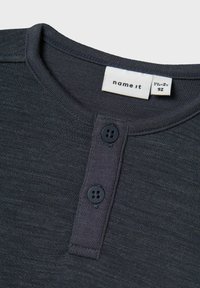 Dunkelgraues Kleinkinder-T-Shirt mit Rundhalsausschnitt und zwei Knöpfen sowie einem weißen Stoffetikett, das die Marke und die Größe 1½-2 Jahre, 92 cm zeigt.