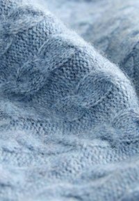 Helleblaue gestrickte Stoff mit auffälligen Zopfmuster, der eine weiche Textur und fuzzy Fasern zeigt. Eine Nahaufnahme hebt das komplizierte Stitching hervor.